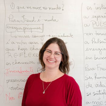 A cheerful female teacher standing in front of a whiteboard with handwriting.