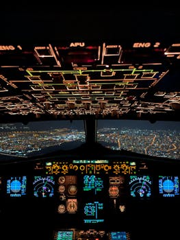 Detailed view of an aircraft cockpit displaying illuminated controls, seen over a nighttime cityscape.